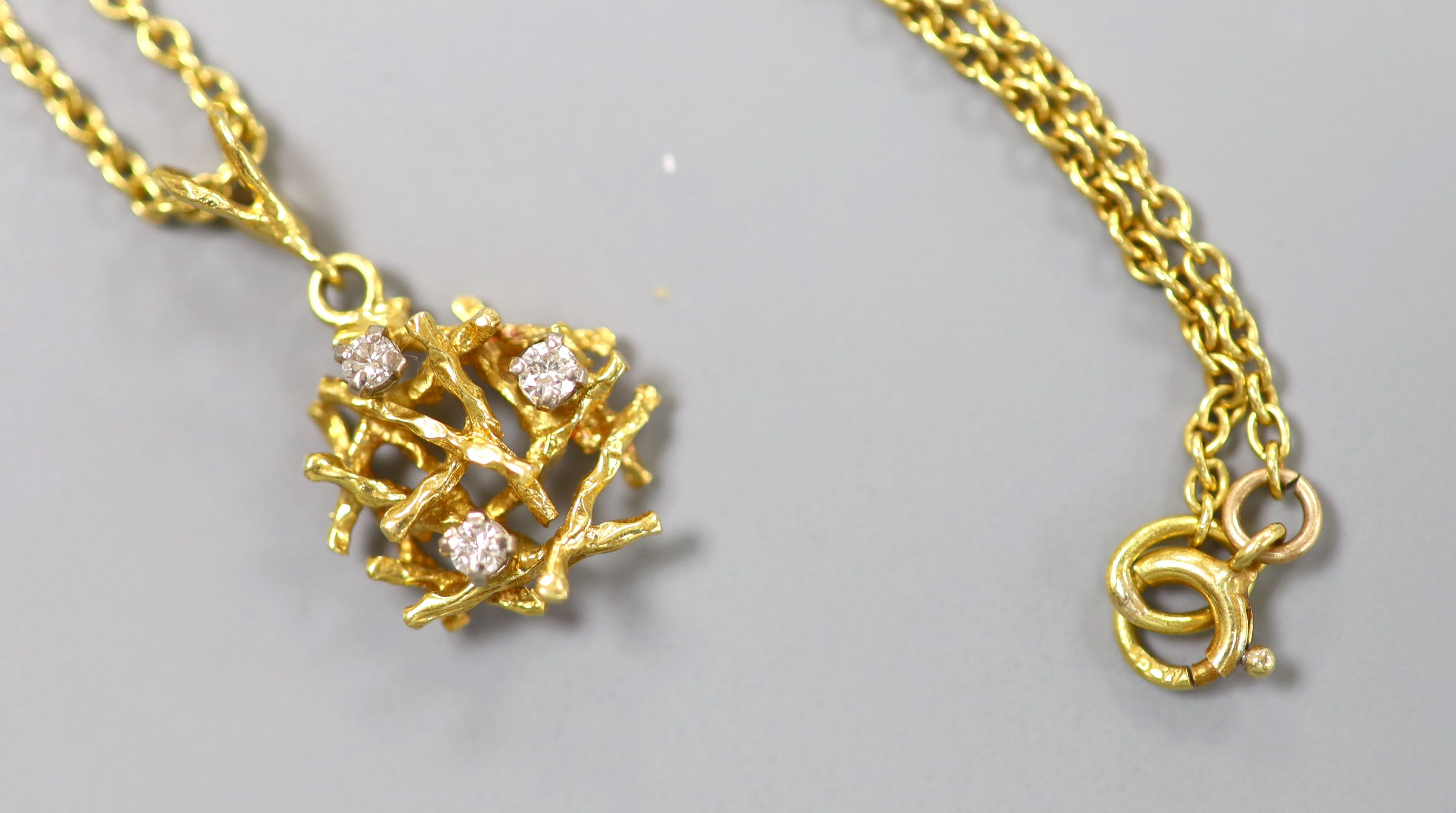 A modern yellow metal and three stone diamond set rustic pendant, 15mm, on a 18ct chain, 45cm